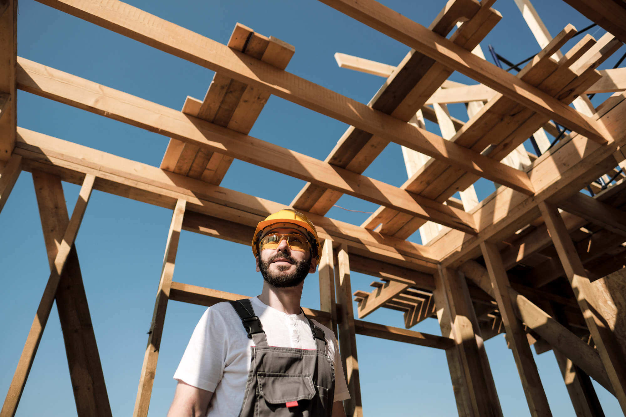 Builder in yellow hard hat standing inside a bare roof frame