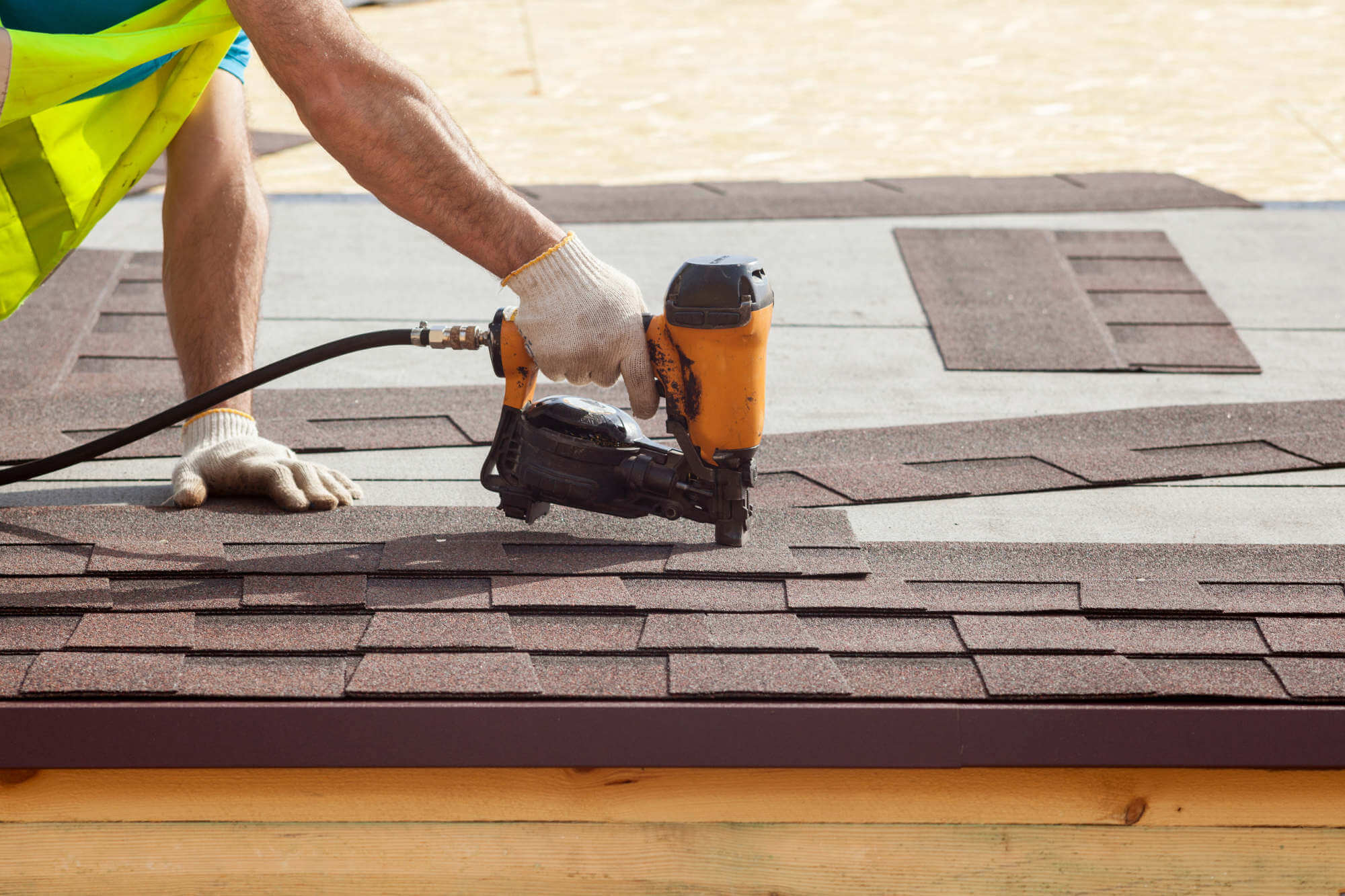 Roofer attaching asphalt shingles with a nail gun